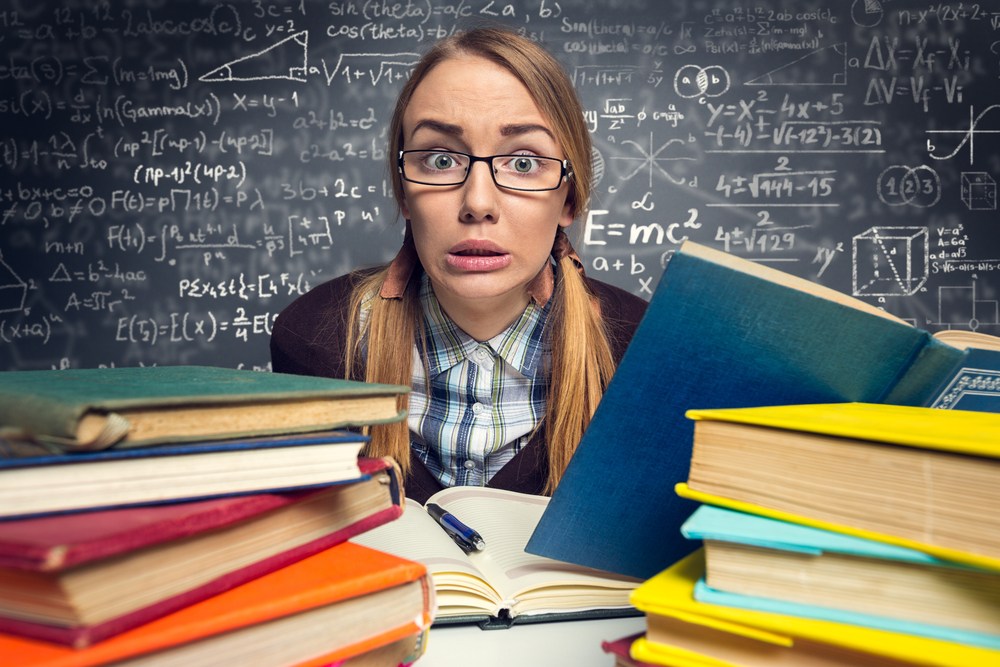 girl between a pile of books studying with black school board behind her